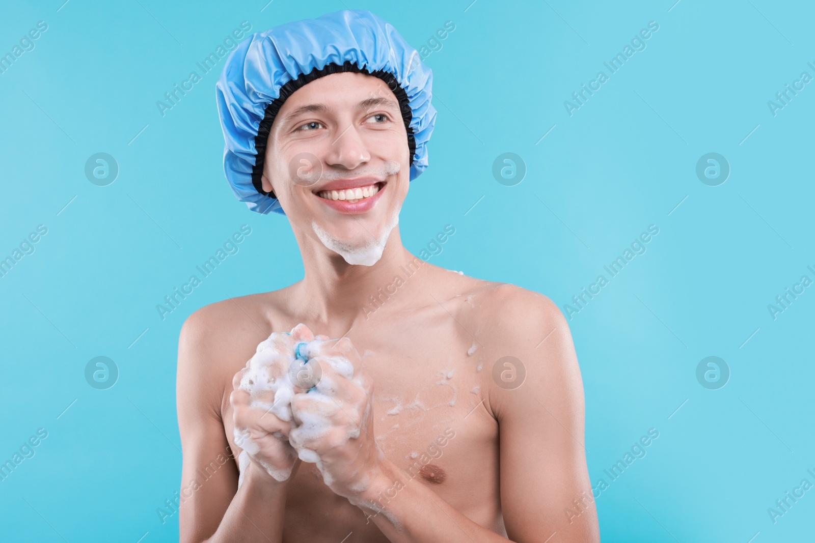 Photo of Man with shower cap and mesh sponge on light blue background