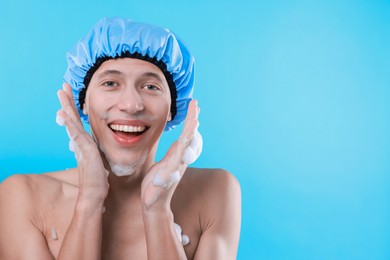 Photo of Man in shower cap covered with soap foam on light blue background, space for text