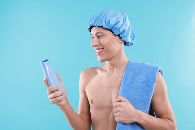 Man with shower cap, shampoo and towel on light blue background