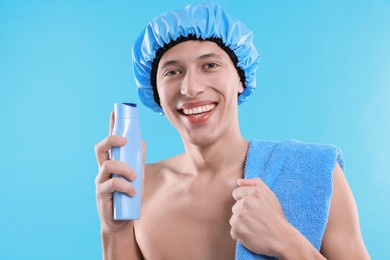 Man with shower cap, shampoo and towel on light blue background