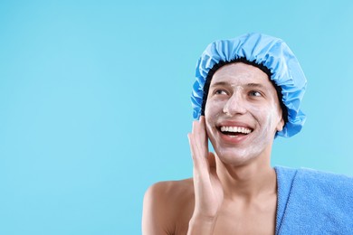 Man in shower cap with cream on his face against light blue background, space for text