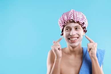 Man in shower cap with cream on his face against light blue background, space for text