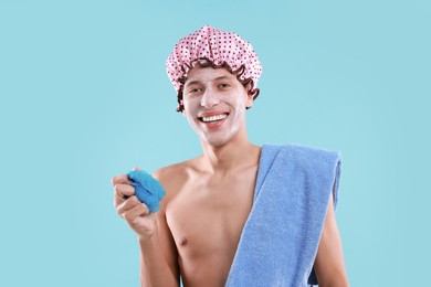 Photo of Man with shower cap, towel and mesh sponge on light blue background