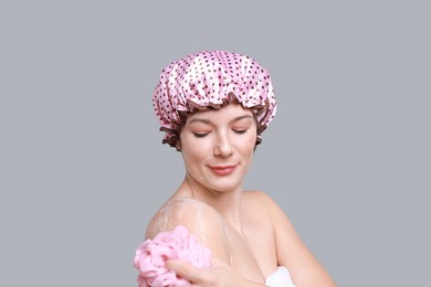 Woman with shower cap and mesh sponge on grey background