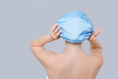 Photo of Woman wearing shower cap on grey background, back view