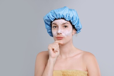 Woman with shower cap and cream on her face against grey background, space for text