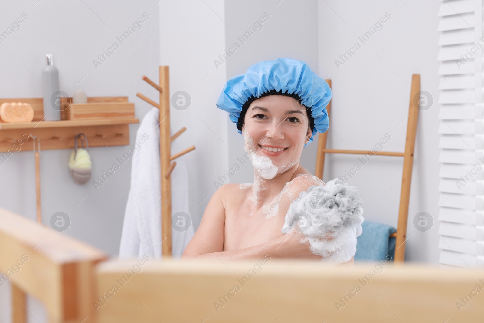 Photo of Woman with cap and mesh sponge taking shower in bathroom