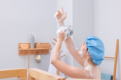 Photo of Woman with cap and mesh sponge taking shower in bathroom