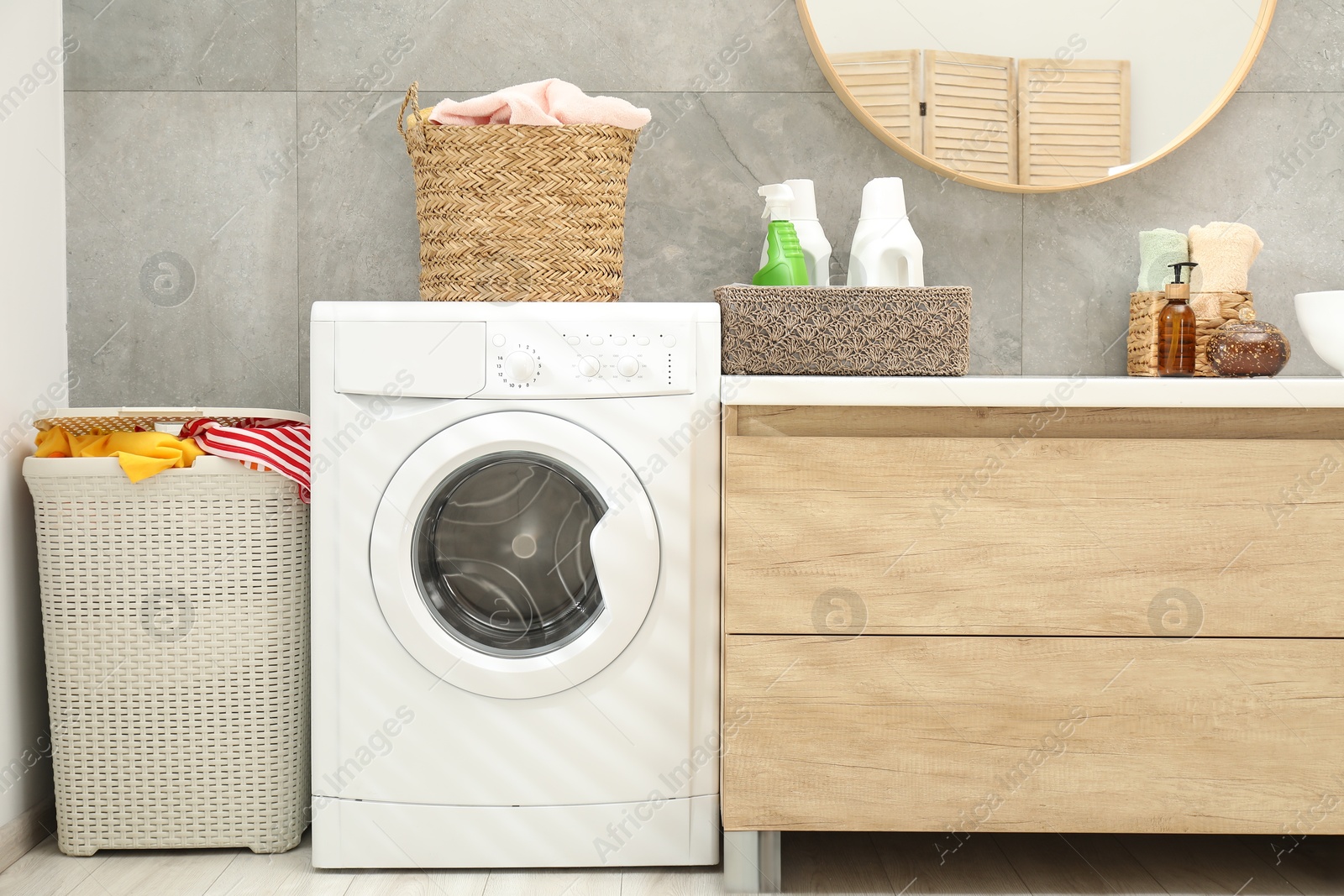 Photo of Wicker baskets full of laundry, washing machine and detergents in bathroom