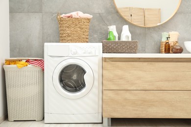 Photo of Wicker baskets full of laundry, washing machine and detergents in bathroom