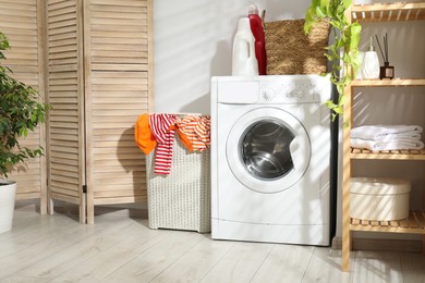 Photo of Wicker basket full of laundry, washing machine and detergents in bathroom