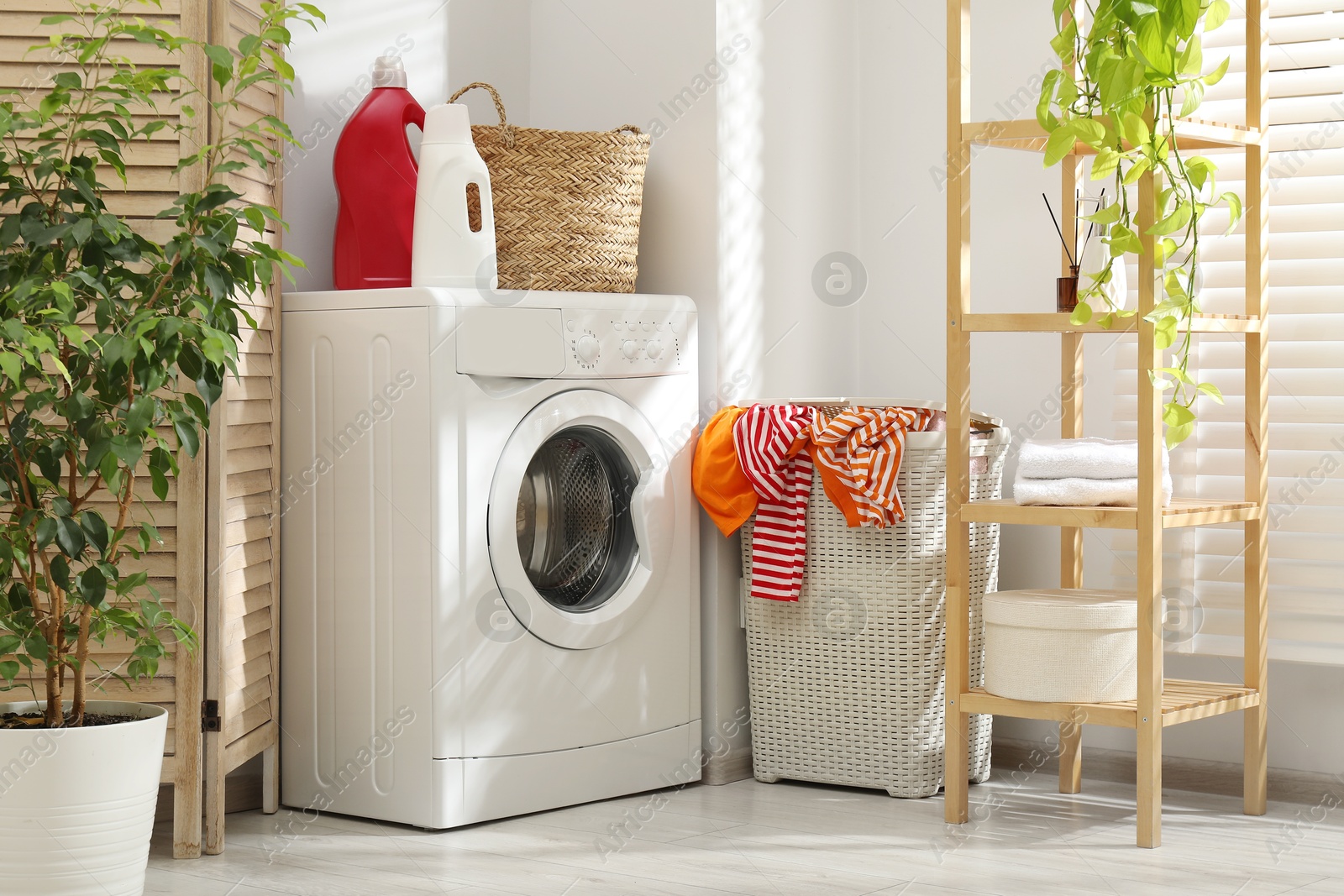 Photo of Wicker basket full of laundry, washing machine and detergents in bathroom