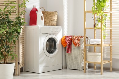 Photo of Wicker basket full of laundry, washing machine and detergents in bathroom