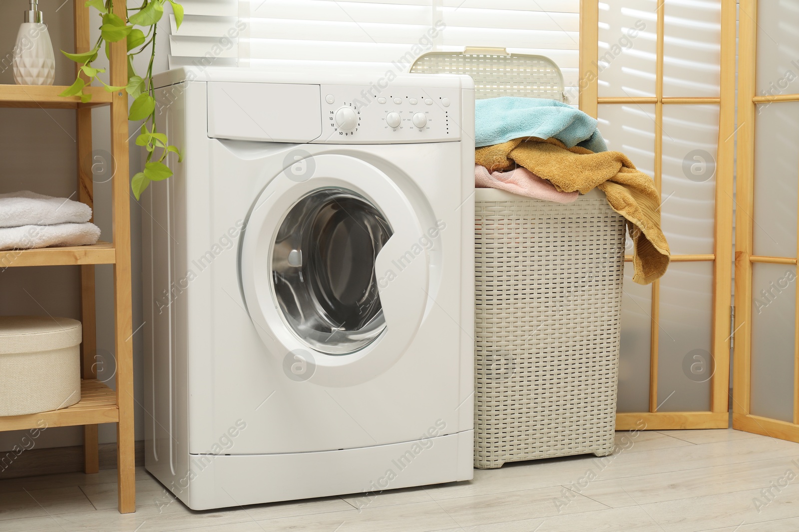 Photo of Wicker basket full of laundry and washing machine in bathroom