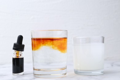 Photo of Iodine starch test. Bottle of aqueous iodine, glasses with water-dissolved iodine and starch solution on white marble table, closeup