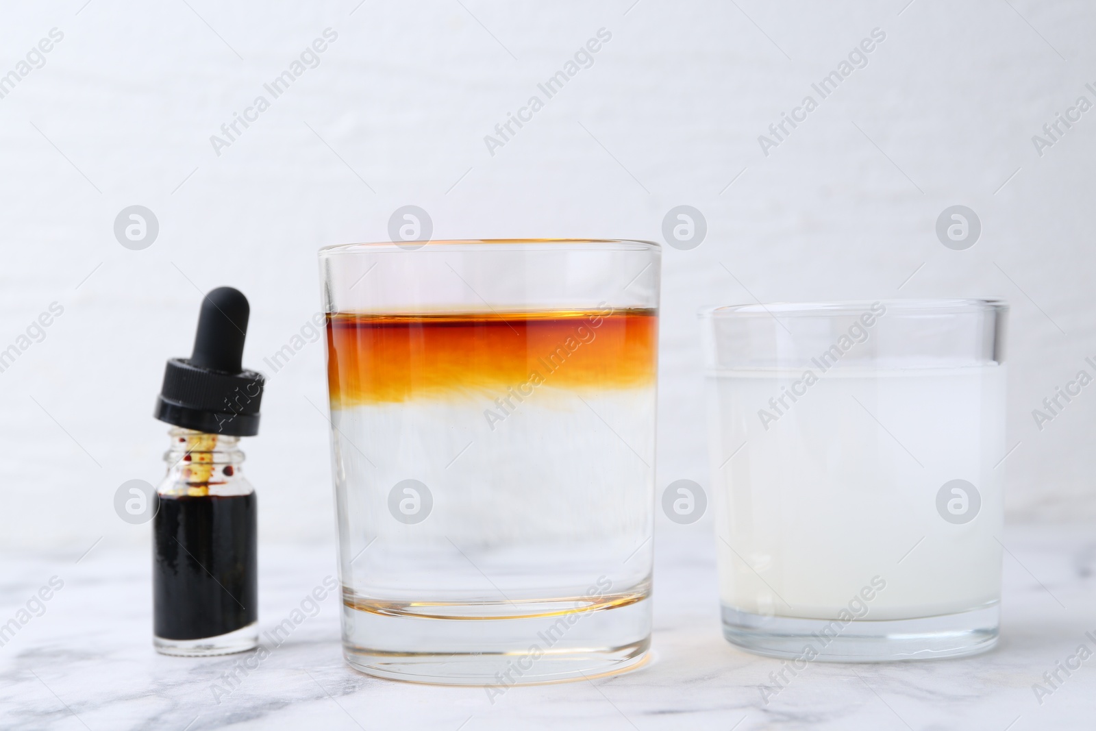 Photo of Iodine starch test. Bottle of aqueous iodine, glasses with water-dissolved iodine and starch solution on white marble table, closeup