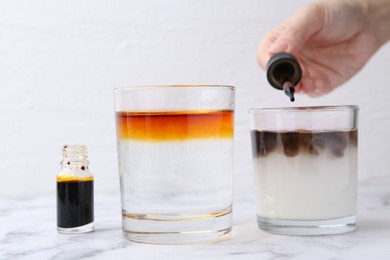 Photo of Iodine starch test. Woman dripping aqueous iodine into glass of water containing starch at white marble table, closeup