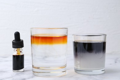 Photo of Iodine starch test. Glasses with liquids of different colors and bottle of aqueous iodine on white marble table, closeup