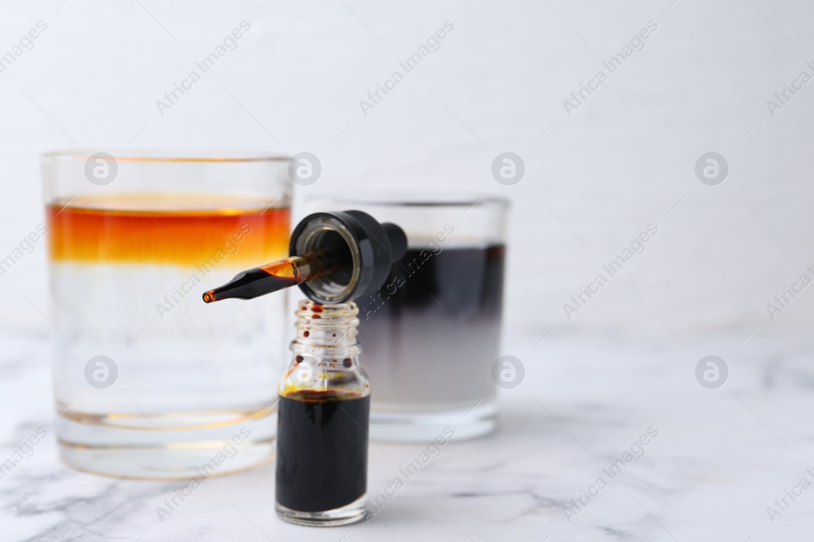 Photo of Bottle of aqueous iodine and glasses with liquids of different colors on white marble table, selective focus. Space for text