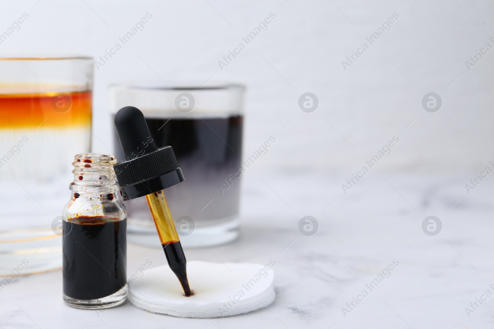 Photo of Bottle of aqueous iodine and glasses with liquids of different colors on white marble table, selective focus. Space for text