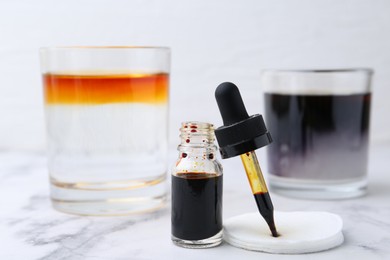 Photo of Bottle of aqueous iodine and glasses with liquids of different colors on white marble table, selective focus