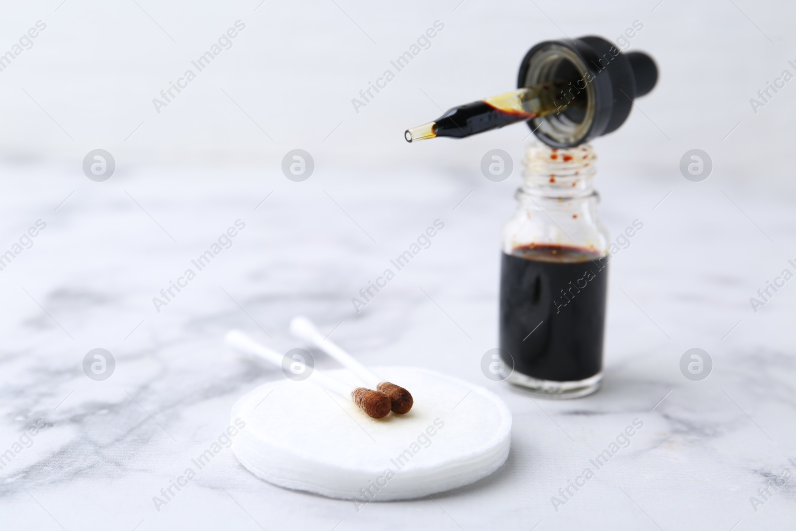 Photo of Bottle of aqueous iodine with pipette and cotton swabs on white marble table, closeup. Space for text