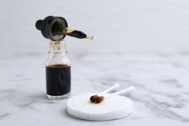 Photo of Bottle of aqueous iodine with pipette and cotton swabs on white marble table, closeup. Space for text