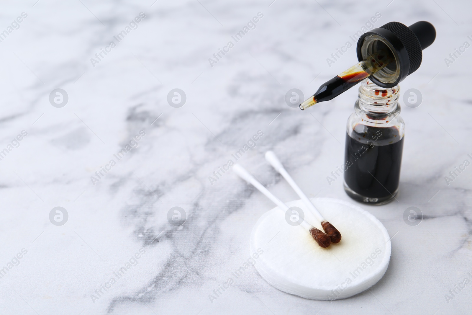 Photo of Bottle of aqueous iodine with pipette and cotton swabs on white marble table, closeup. Space for text