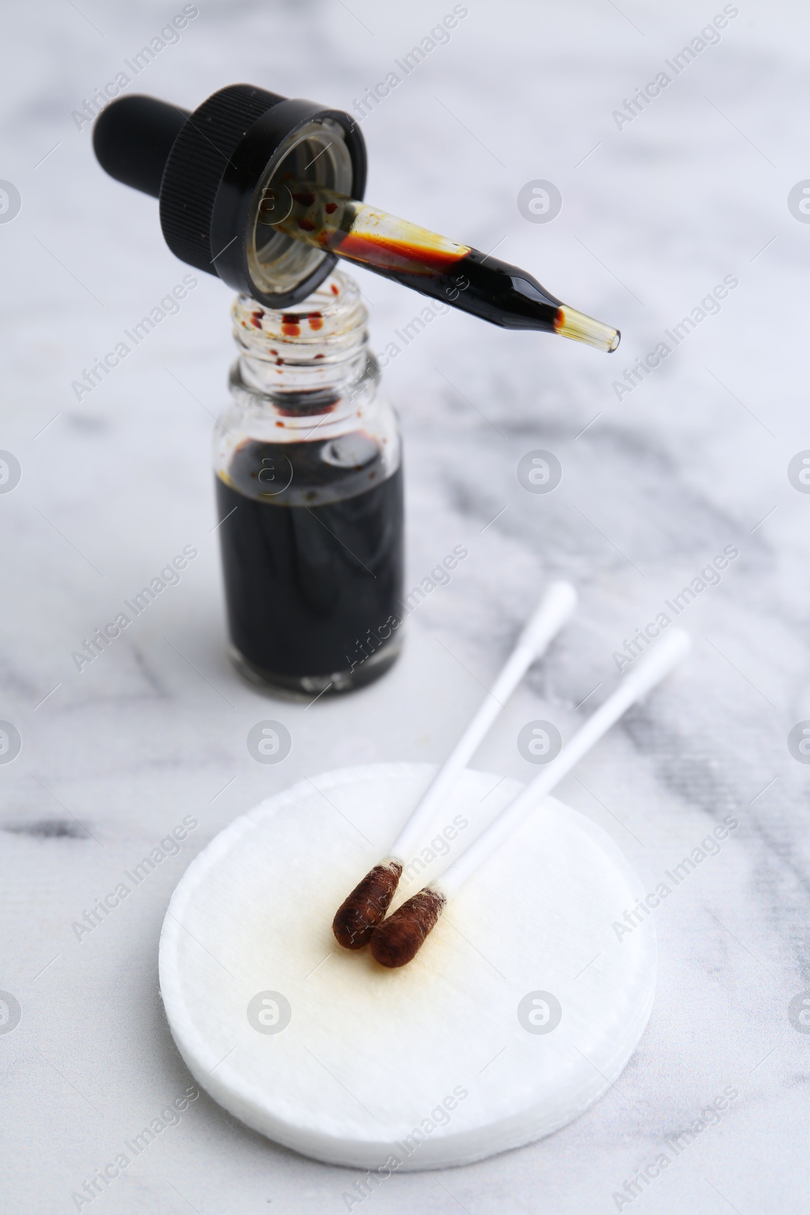 Photo of Bottle of aqueous iodine with pipette and cotton swabs on white marble table, closeup