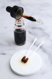 Photo of Bottle of aqueous iodine with pipette and cotton swabs on white marble table, closeup