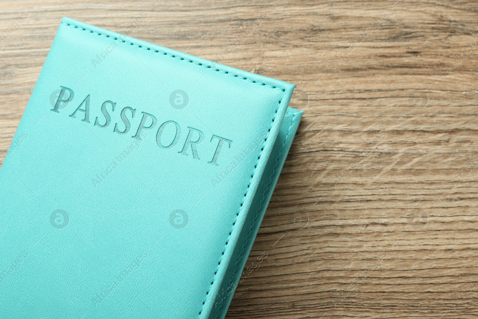 Photo of Passport in turquoise cover on wooden table, top view. Space for text