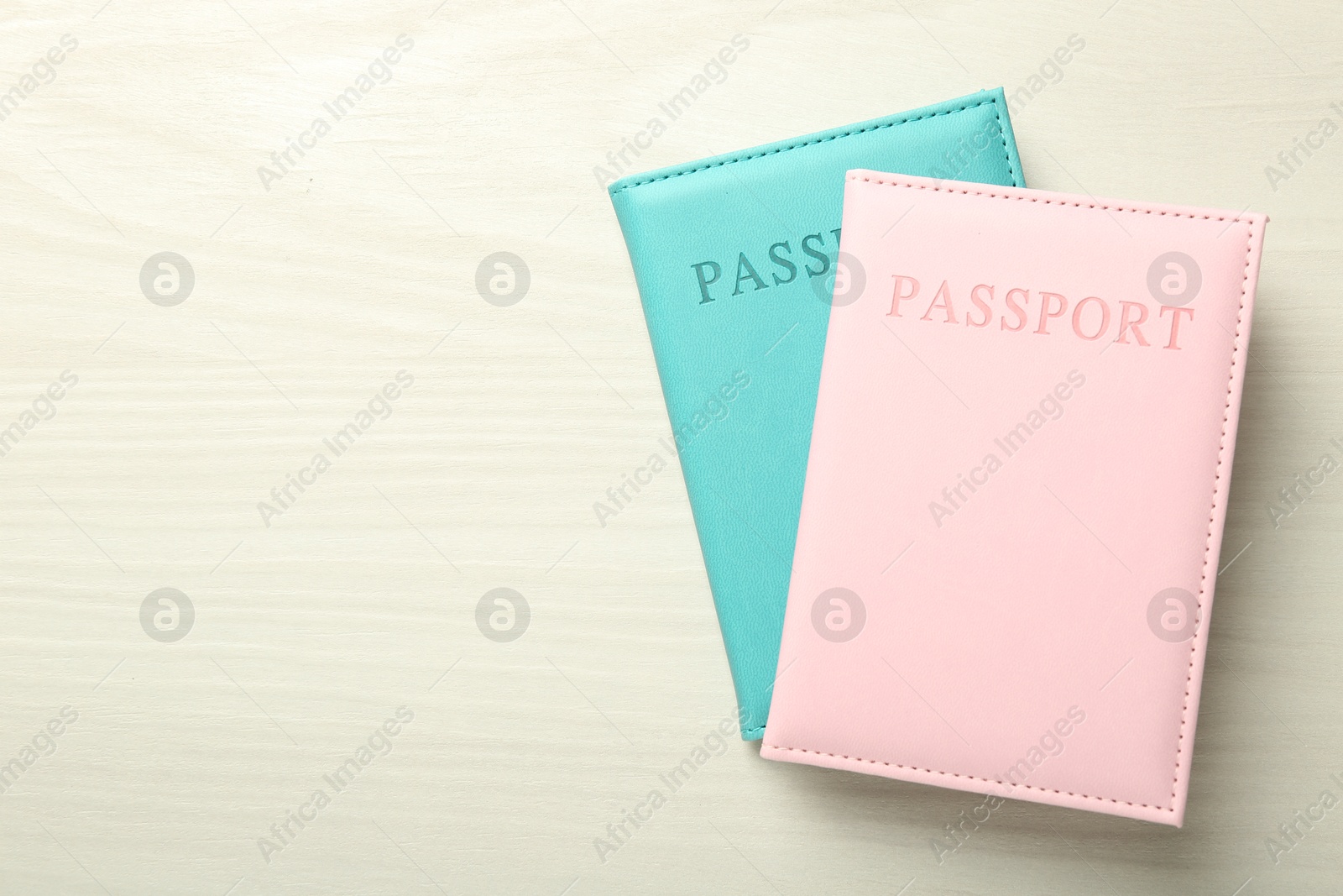 Photo of Two passports in bright covers on white wooden table, top view. Space for text