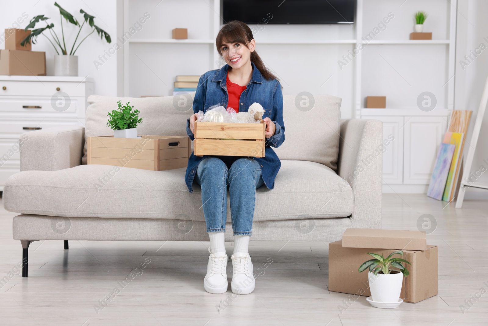 Photo of Happy woman holding wooden crate with stuff in new apartment. Housewarming party