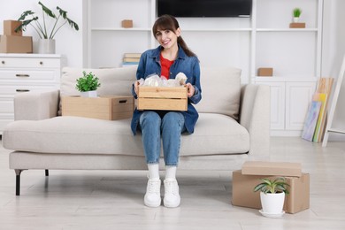 Happy woman holding wooden crate with stuff in new apartment. Housewarming party