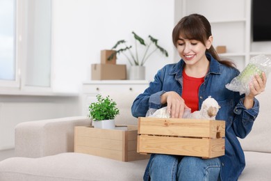 Photo of Happy woman holding wooden crate with stuff in new apartment. Housewarming party