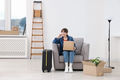 Photo of Happy woman with moving boxes and suitcase in new apartment. Housewarming party