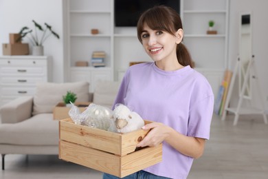 Happy woman holding wooden crate with stuff in new apartment. Housewarming party