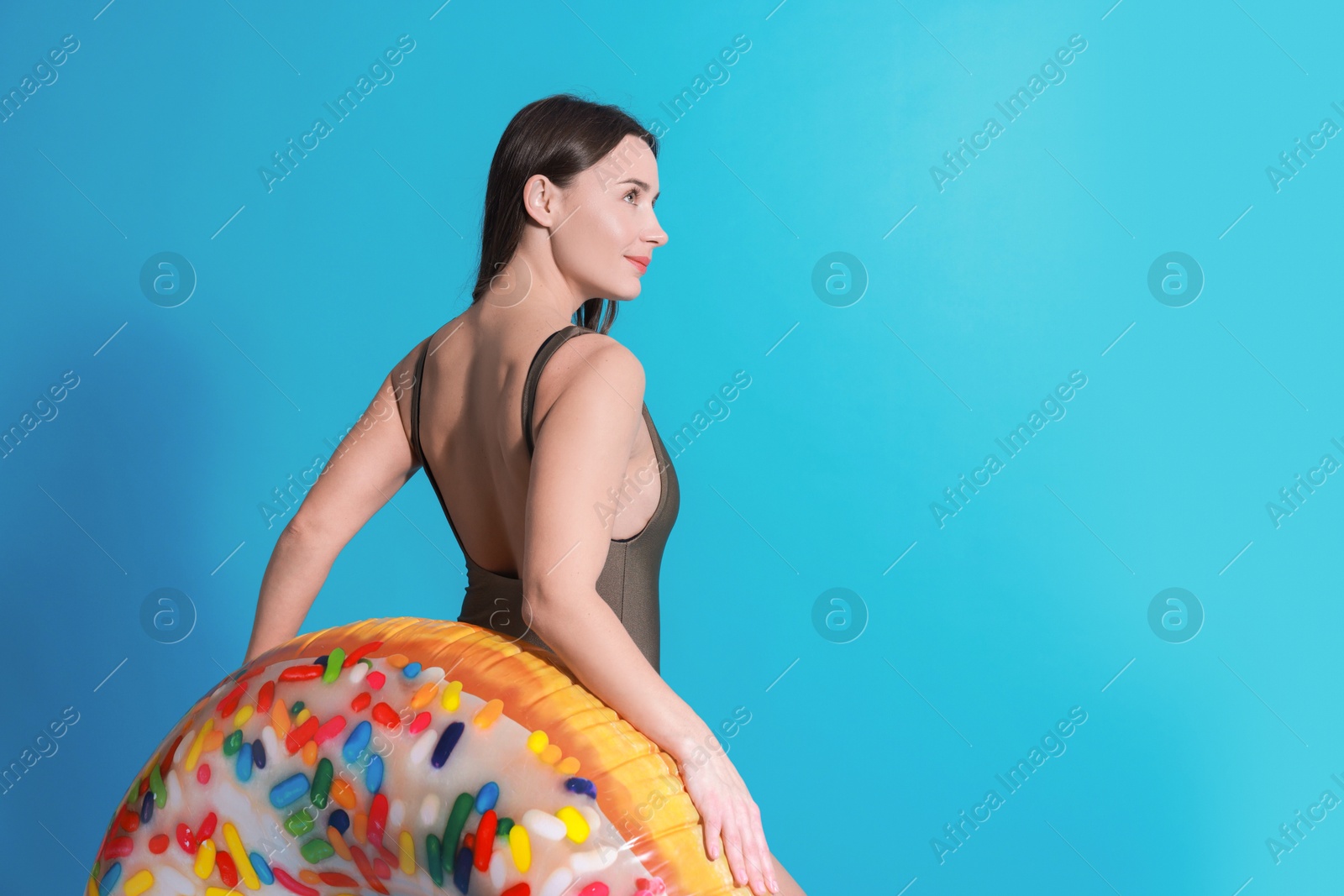 Photo of Beautiful woman in swimsuit with inflatable ring on light blue background. Space for text