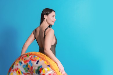 Photo of Beautiful woman in swimsuit with inflatable ring on light blue background. Space for text