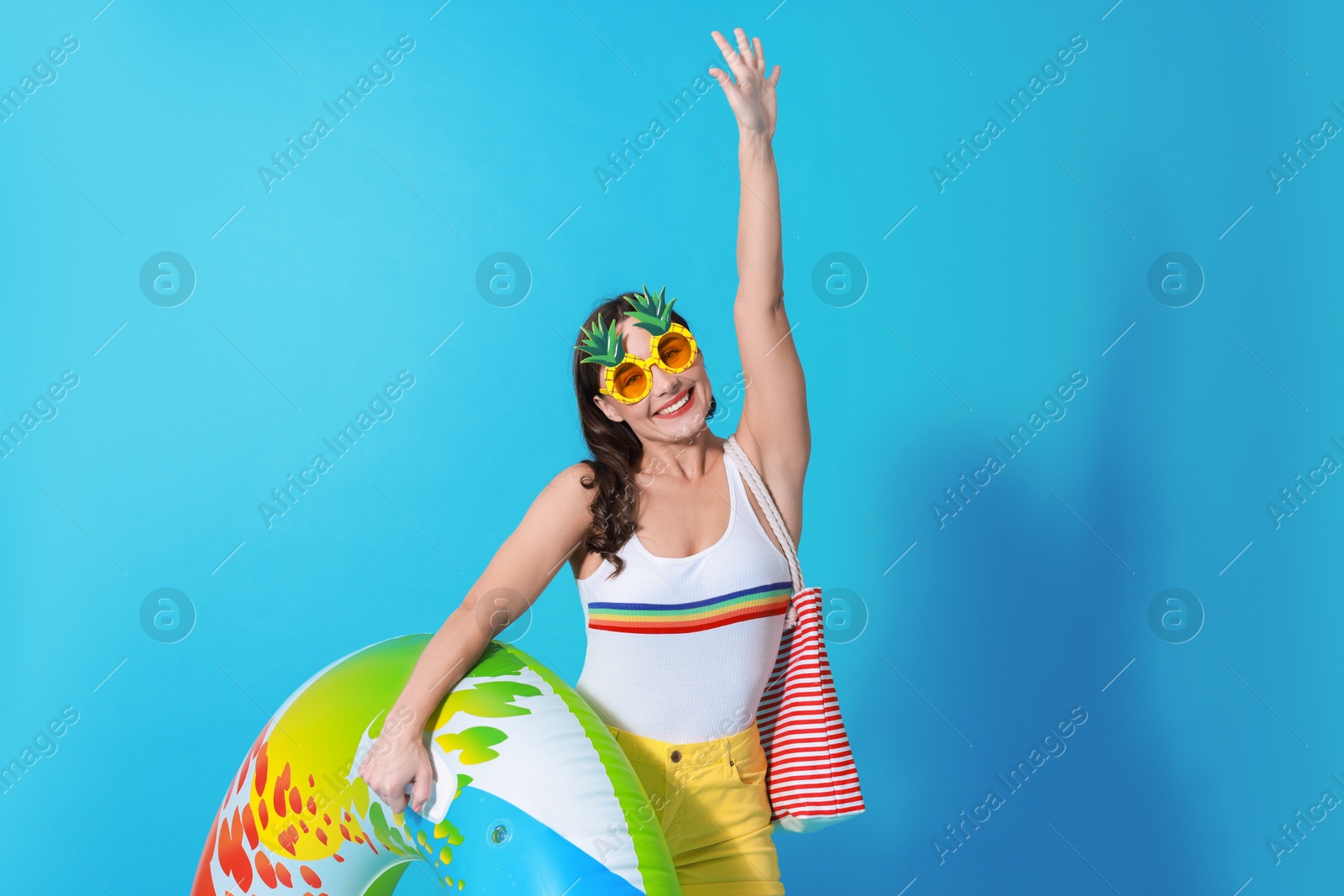 Photo of Beautiful woman wearing swimsuit and funny sunglasses with inflatable ring on light blue background