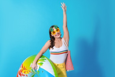 Photo of Beautiful woman wearing swimsuit and funny sunglasses with inflatable ring on light blue background