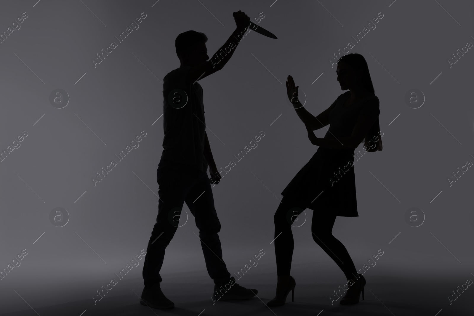 Photo of Domestic violence. Silhouette of man with knife threatening his wife on grey background