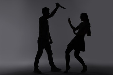 Domestic violence. Silhouette of man with knife threatening his wife on grey background