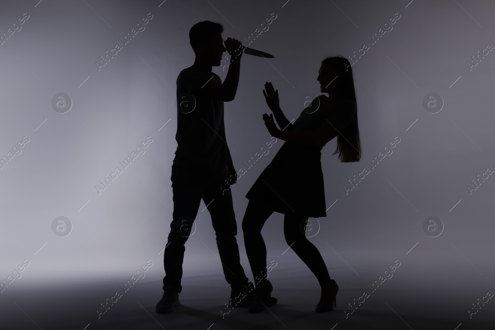 Photo of Domestic violence. Silhouette of man with knife threatening his wife on grey background