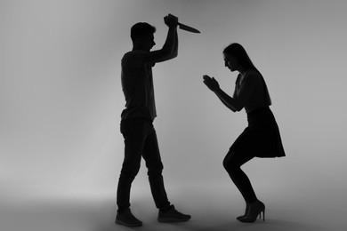 Domestic violence. Silhouette of man with knife threatening his wife on grey background