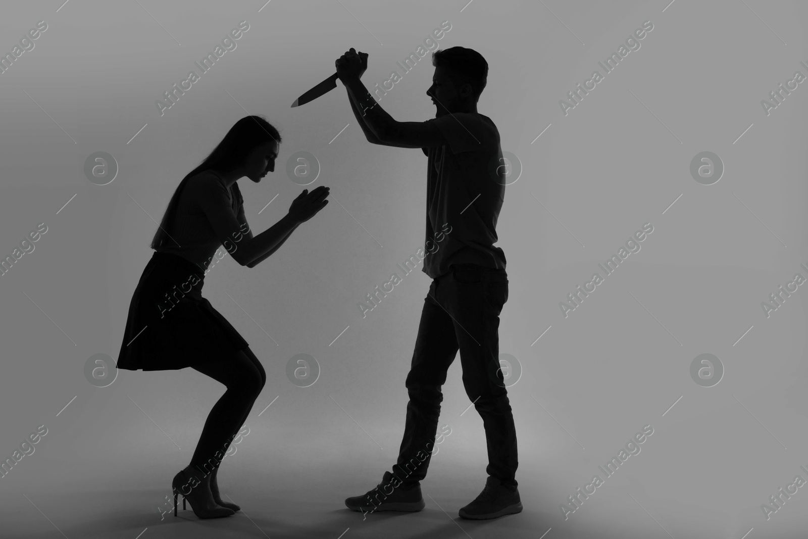 Photo of Domestic violence. Silhouette of man with knife threatening his wife on grey background