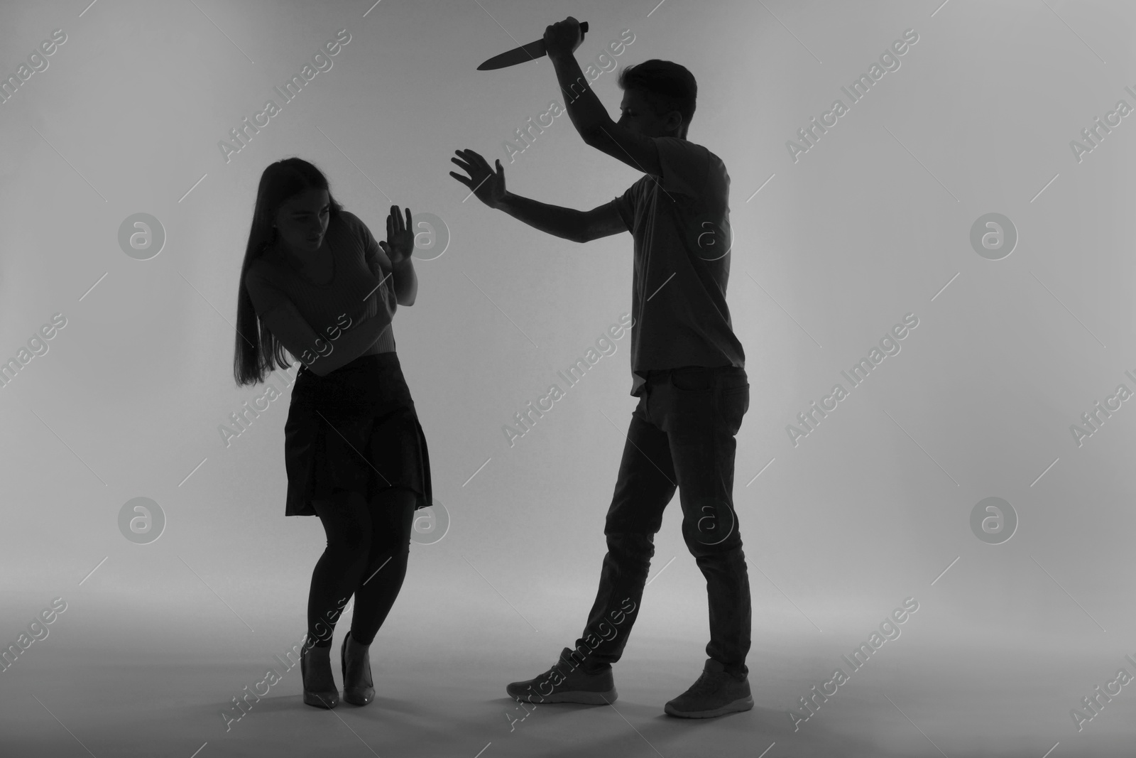 Photo of Domestic violence. Silhouette of man with knife threatening his wife on grey background