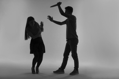 Domestic violence. Silhouette of man with knife threatening his wife on grey background