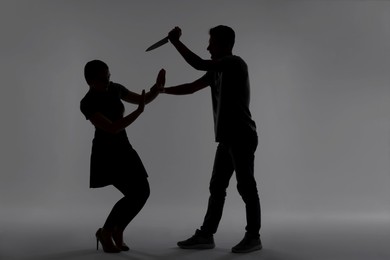 Photo of Domestic violence. Silhouette of man with knife threatening his wife on grey background