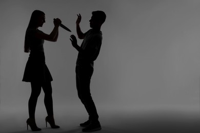 Photo of Domestic violence. Silhouette of woman with knife threatening her husband on grey background, space for text